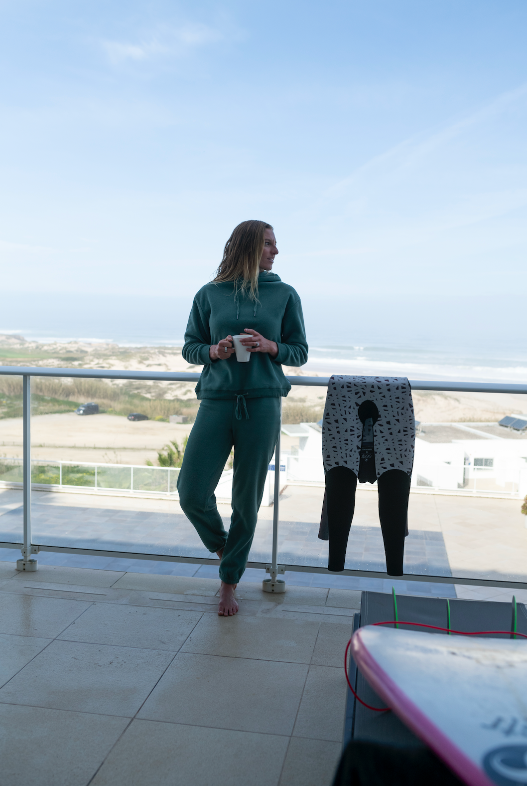 Person standing on a balcony with a scenic view, holding a phone.